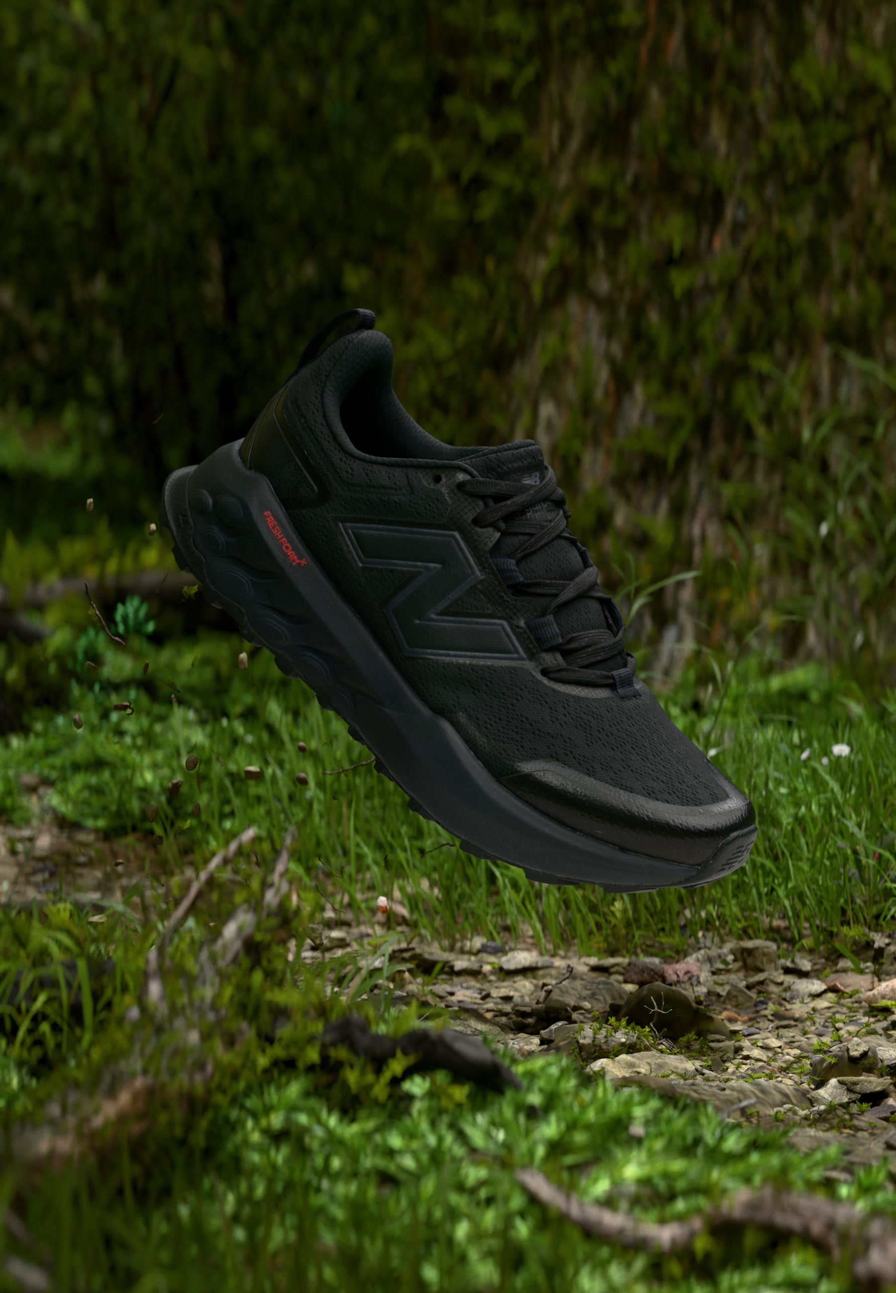 Zapatilla deportiva negra con suela gruesa y logo "N", flotando sobre un suelo forestal rocoso cubierto de musgo con vegetación al fondo.