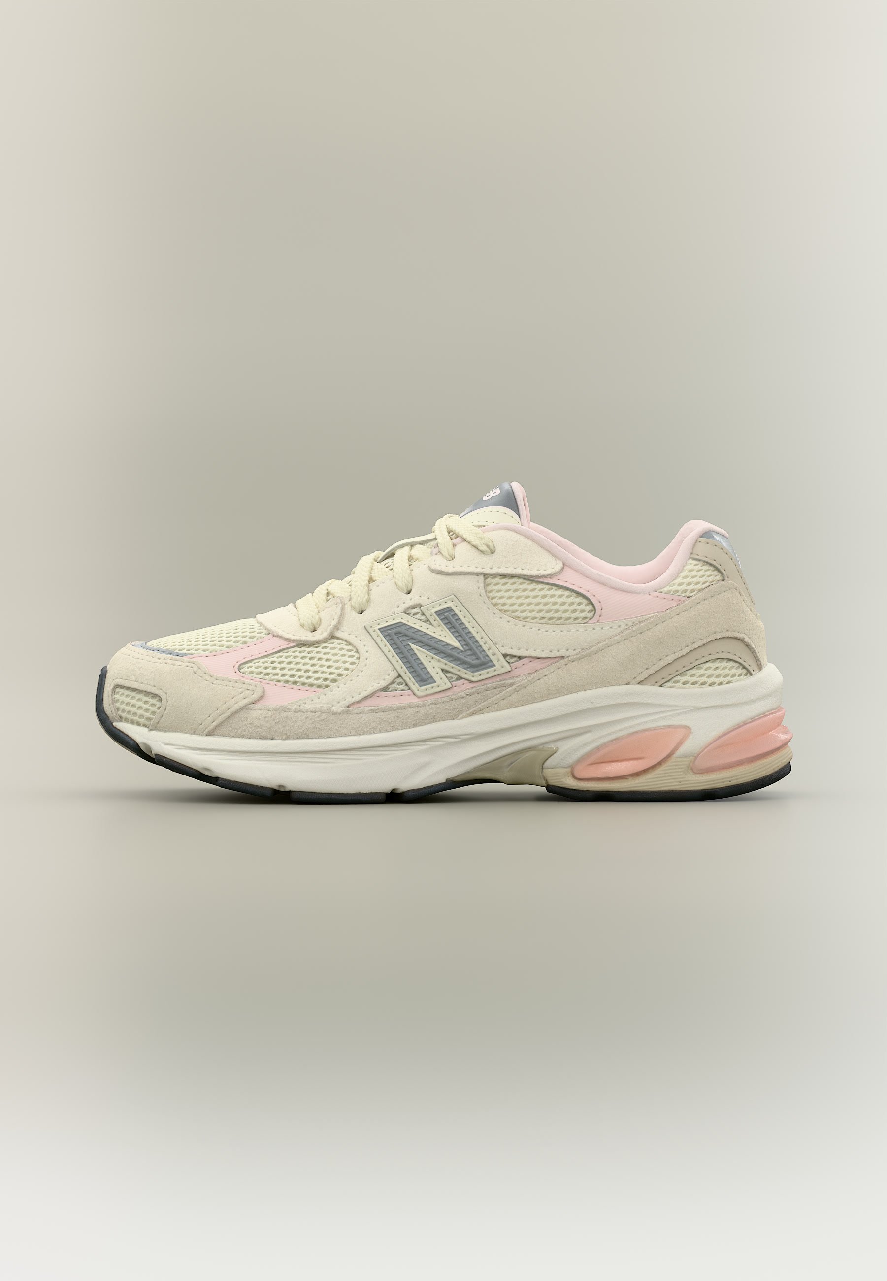 Zapatilla New Balance de color beige y rosa pálido con paneles de malla, superposiciones de ante y suela acolchada vista desde el lado izquierdo sobre un fondo neutro.