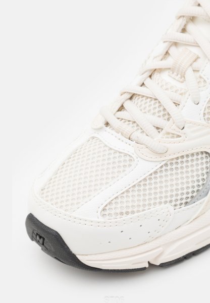 Primer plano de un zapato deportivo blanco con paneles de malla, superposiciones de cuero, cordones blancos y una suela de goma negra en la punta.