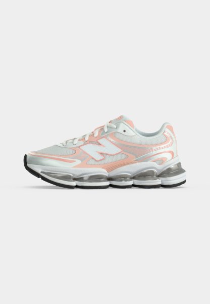 Zapatilla deportiva blanca y melocotón con cordones delanteros, parte superior de malla y suela gruesa transparente segmentada.