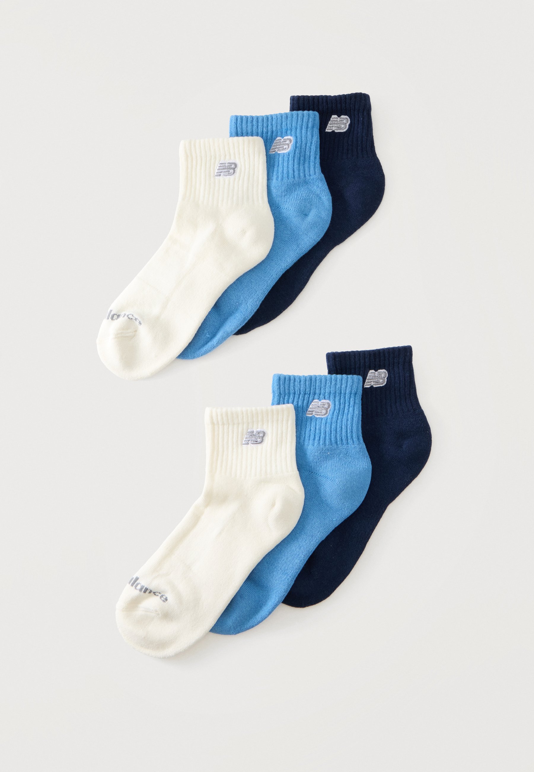Dos juegos de tres calcetines tobilleros cada uno, en blanco, azul claro y azul marino, dispuestos sobre un fondo blanco liso.