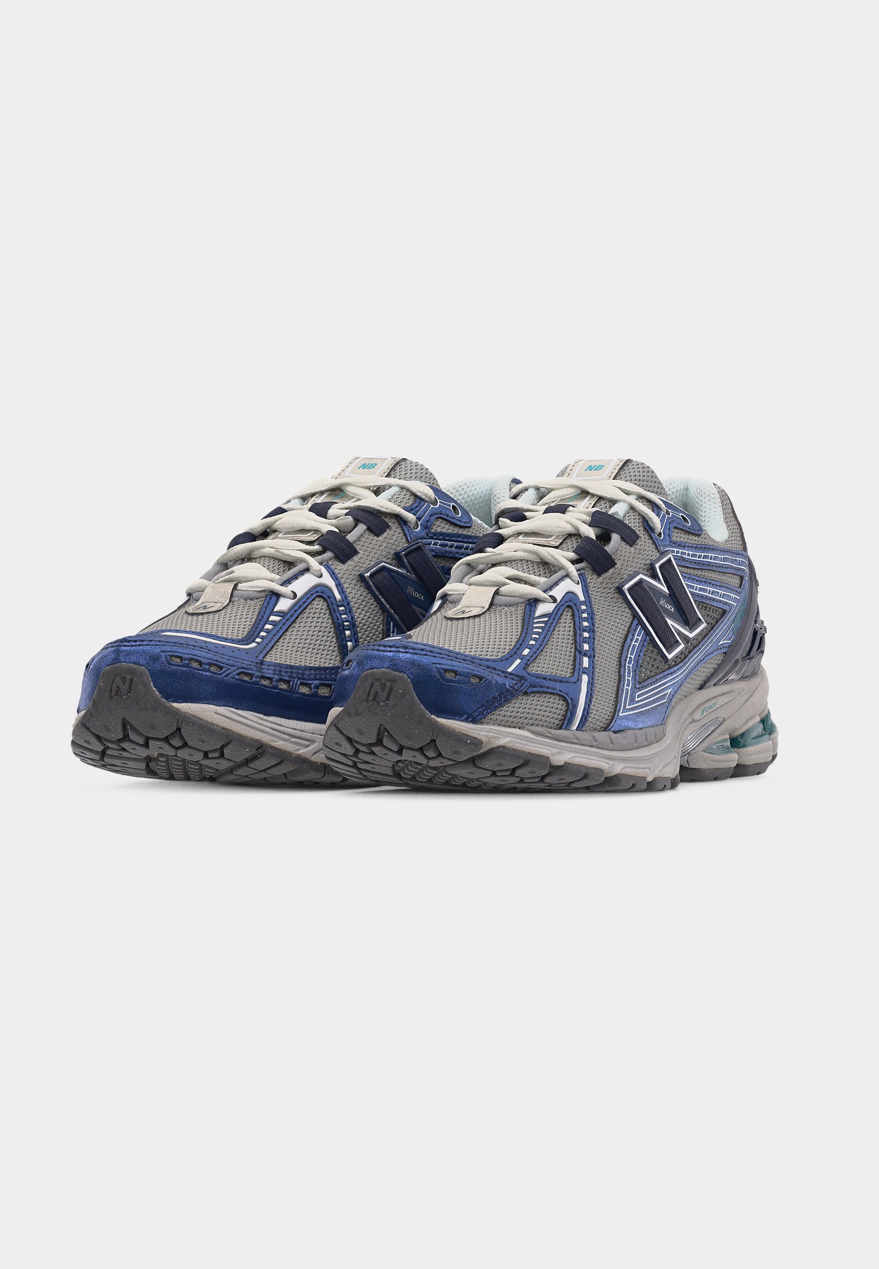 Par de zapatillas de running New Balance en gris y azul con cordones blancos, paneles de malla y suelas de goma texturizadas, sobre un fondo blanco.