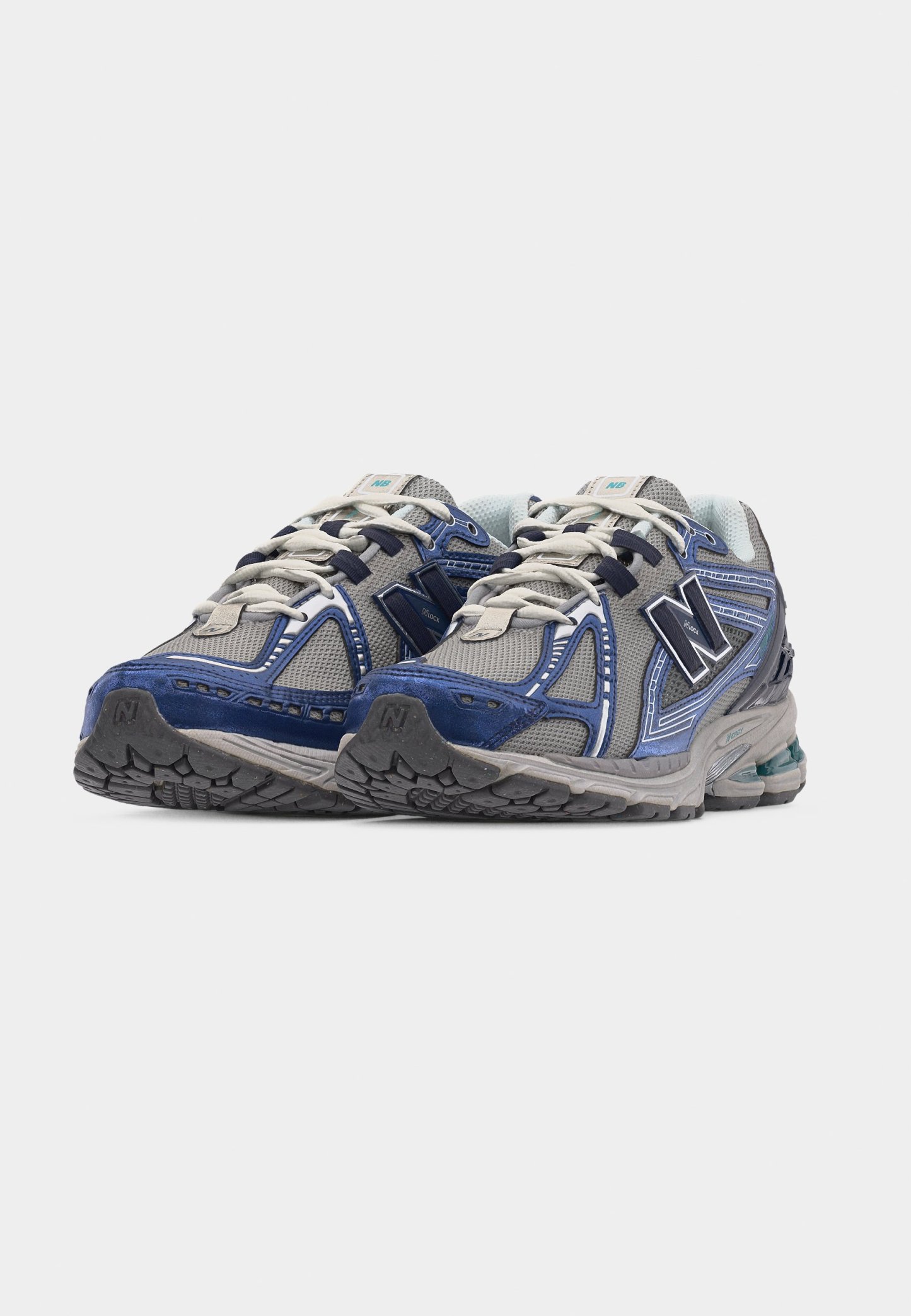 Par de zapatillas de running New Balance en gris y azul con cordones blancos, paneles de malla y suelas de goma texturizadas, sobre un fondo blanco.