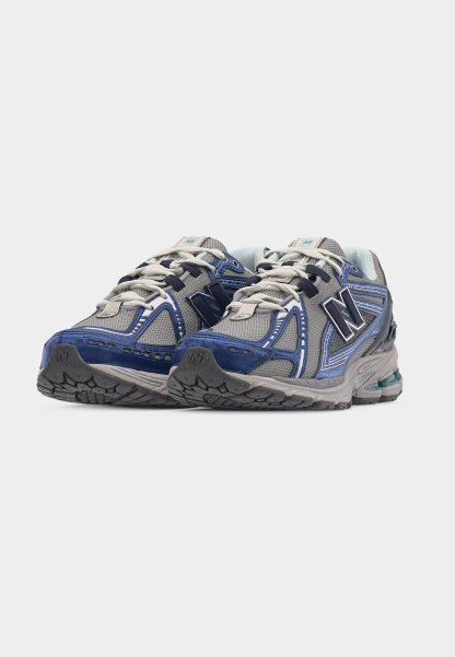 Par de zapatillas de running New Balance en gris y azul con cordones blancos, paneles de malla y suelas de goma texturizadas, sobre un fondo blanco.