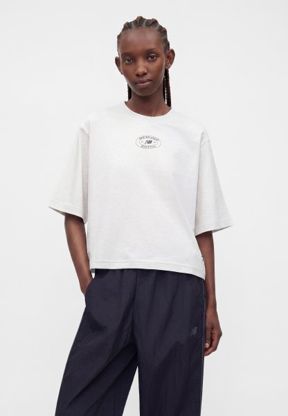 Mujer con cabello trenzado lleva una camiseta blanca oversize de New Balance y pantalones sueltos de color azul marino oscuro, de pie frente a un fondo blanco liso.