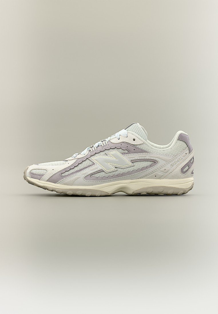 Zapatilla New Balance blanca y gris claro con paneles de malla y ante, cierre de cordones y suela de goma texturizada, vista de perfil.