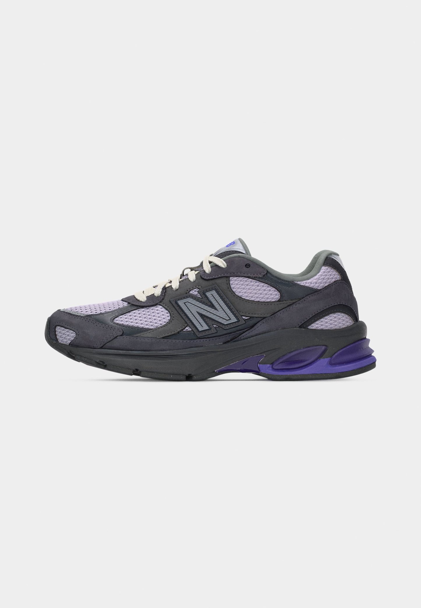 Zapatilla deportiva en tonos gris oscuro y púrpura con tejido de malla, cordones blancos y logotipo "N" de la marca en el lateral, vista de perfil.