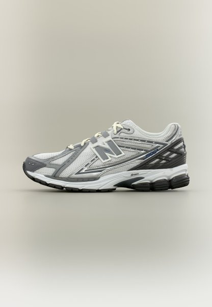 Zapatilla de running New Balance blanca y gris con parte superior de malla, logo de la marca, suela acolchada y suela exterior negra, mostrada sobre fondo neutro.