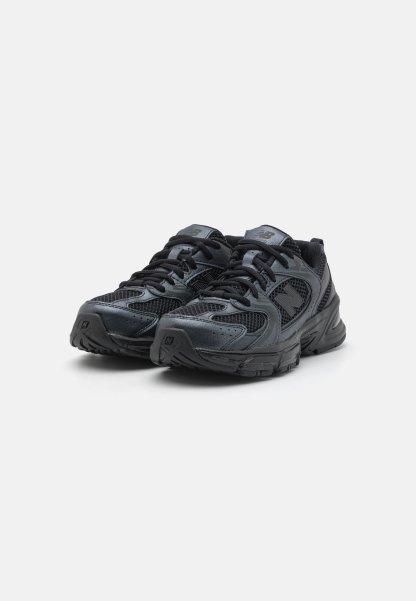 Zapatillas deportivas negras con parte superior de malla y sintético, collar acolchado, cordones y suela de goma texturizada, con un logo en la lengüeta.