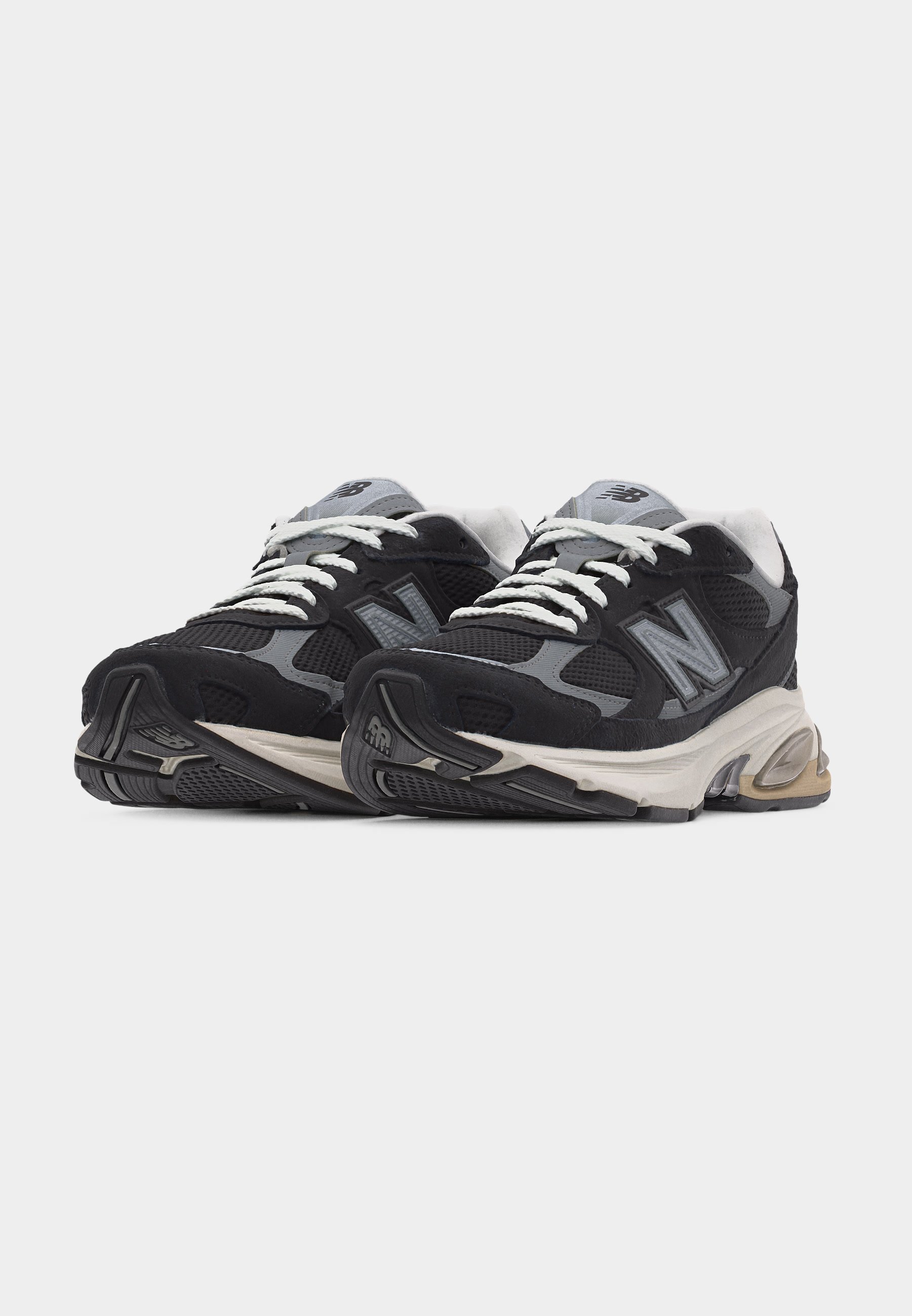 Par de zapatillas deportivas New Balance negras y grises con cordones blancos y suelas acolchadas sobre un fondo liso.