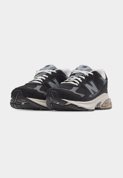 Par de zapatillas deportivas New Balance negras y grises con cordones blancos y suelas acolchadas sobre un fondo liso.