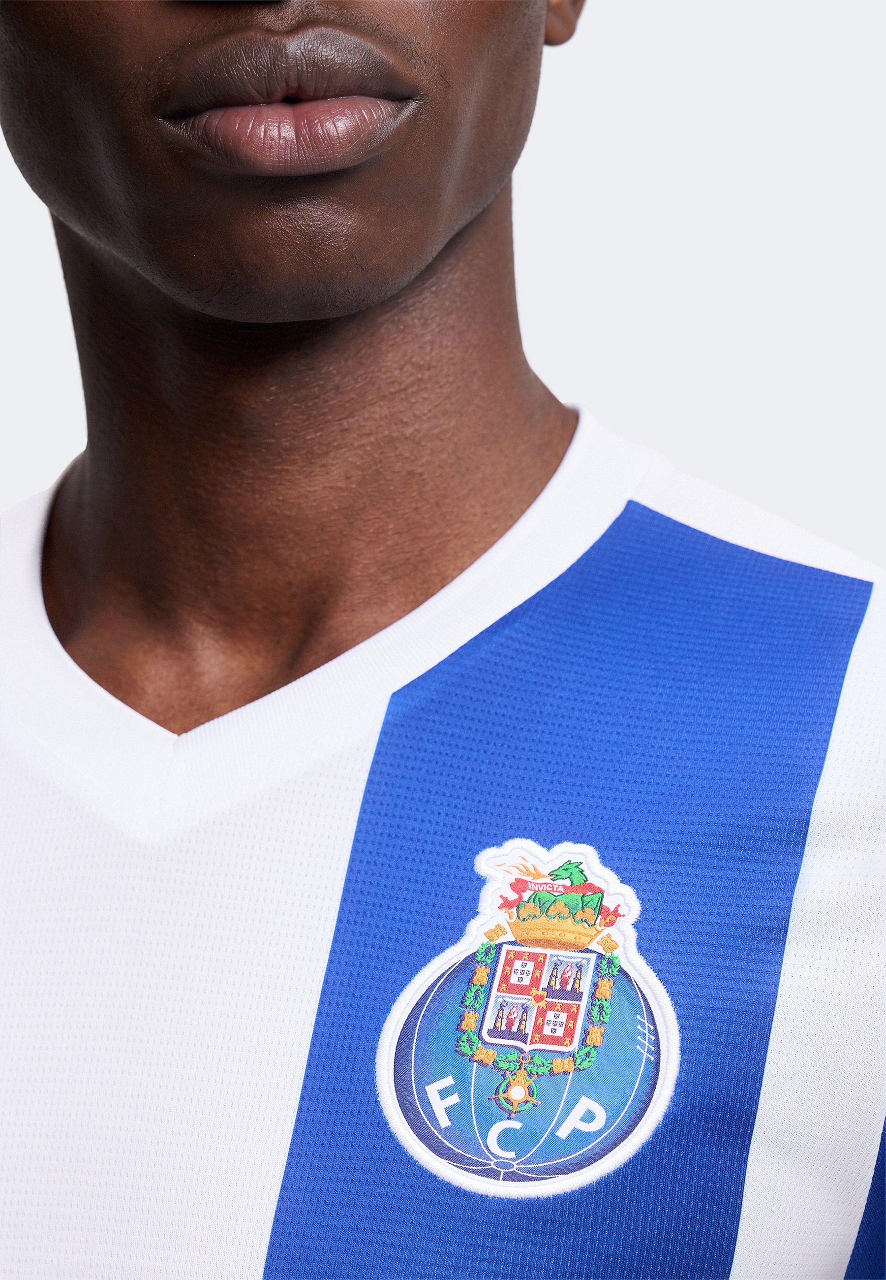 Primer plano de una persona que lleva una camiseta deportiva blanca y azul a rayas con el escudo del club de fútbol FC Porto en el pecho.