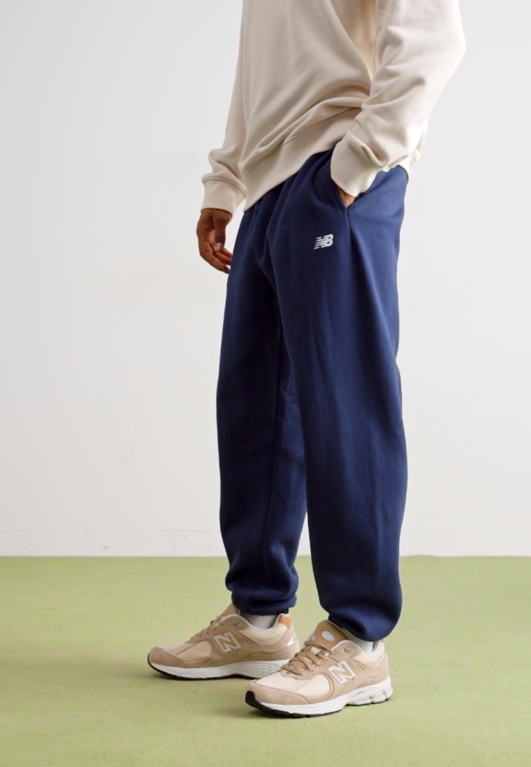 Pantalones de chándal azul marino con cintura elástica y bolsillos laterales; combinados con zapatillas beige que tienen un logo blanco y detalles de malla.