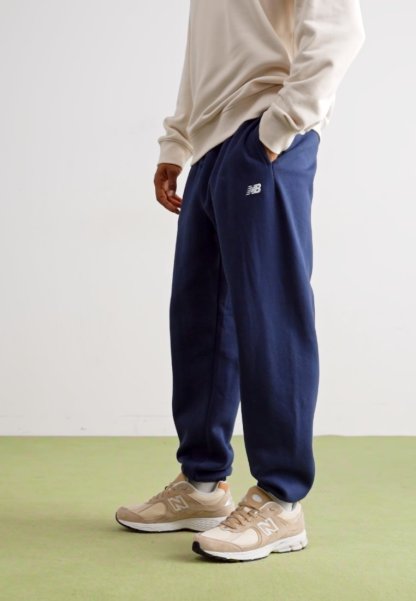 Pantalones de chándal azul marino con cintura elástica y bolsillos laterales; combinados con zapatillas beige que tienen un logo blanco y detalles de malla.