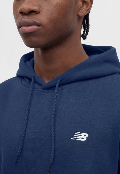 Joven con el pelo trenzado que lleva una sudadera con capucha azul marino de New Balance, mostrando la parte superior del pecho y parte del rostro sobre un fondo liso.