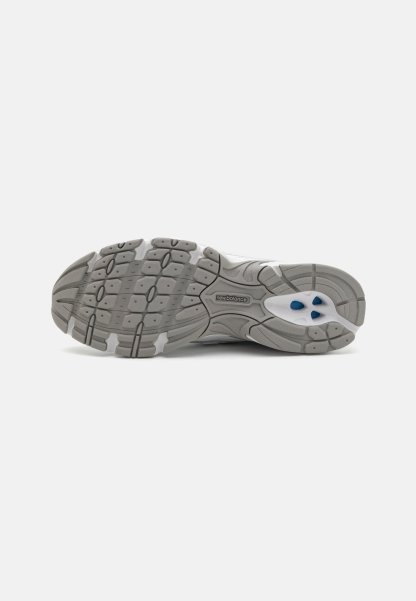 Suela de goma gris con patrón de tracción texturizado; presenta acentos blancos y detalles azules. Logotipo de la marca visible en el lateral.