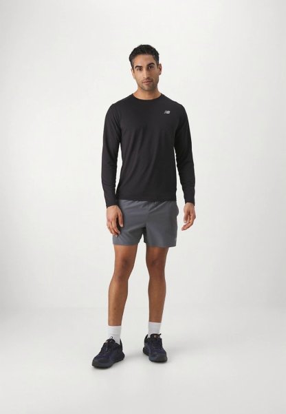Camisa negra de manga larga y pantalones cortos deportivos grises. Logo negro en la camisa. Zapatillas deportivas con calcetines blancos. Diseño simple y ajustado.