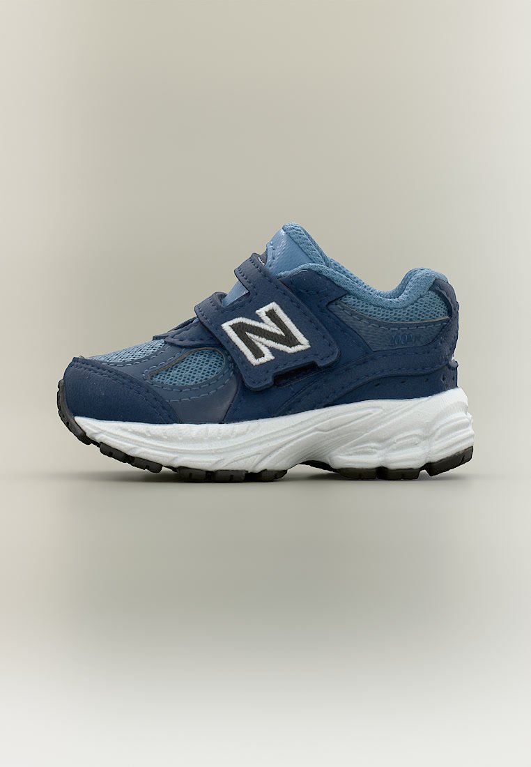 Zapatilla para niños en azul y azul marino con suela blanca, parte superior de malla y cuero, y dos tiras de Velcro con un logo blanco "N" en el lateral.