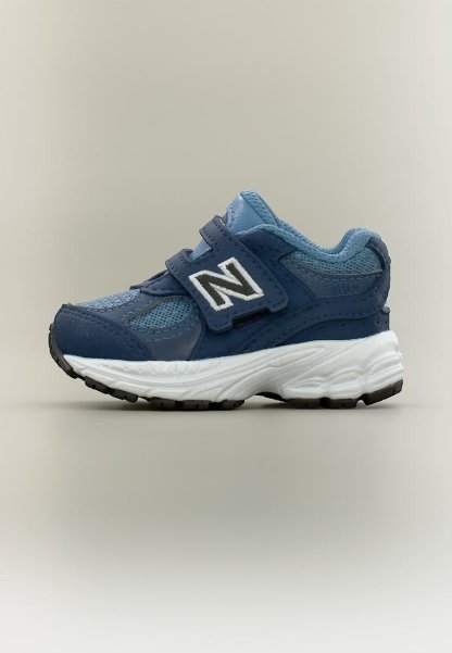 Zapatilla para niños en azul y azul marino con suela blanca, parte superior de malla y cuero, y dos tiras de Velcro con un logo blanco "N" en el lateral.