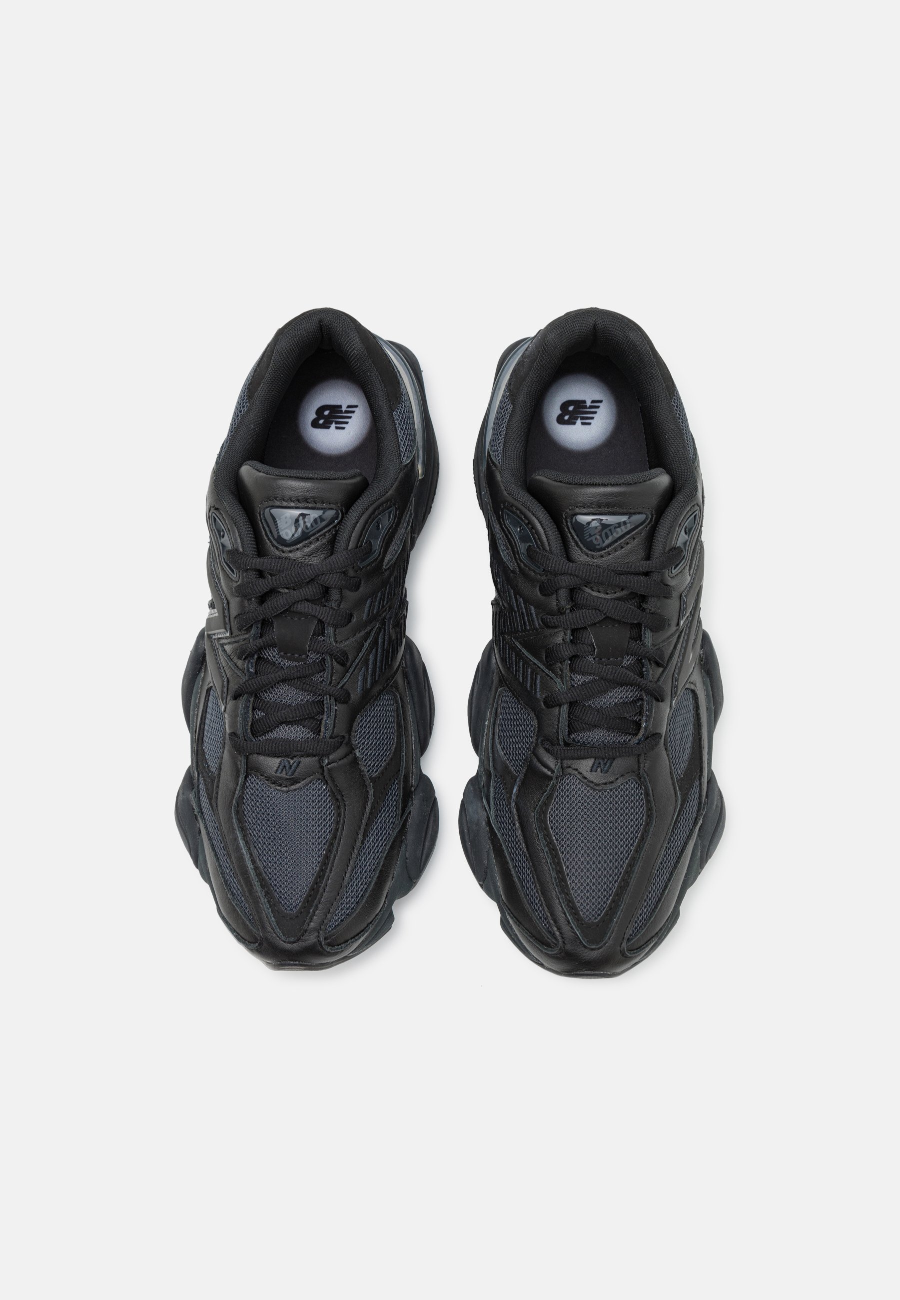 Zapatillas deportivas negras con parte superior de malla y sintético, que cuentan con una suela gruesa, acentos texturizados y un logotipo prominente en la lengüeta.