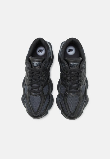 Zapatillas deportivas negras con parte superior de malla y sintético, que cuentan con una suela gruesa, acentos texturizados y un logotipo prominente en la lengüeta.