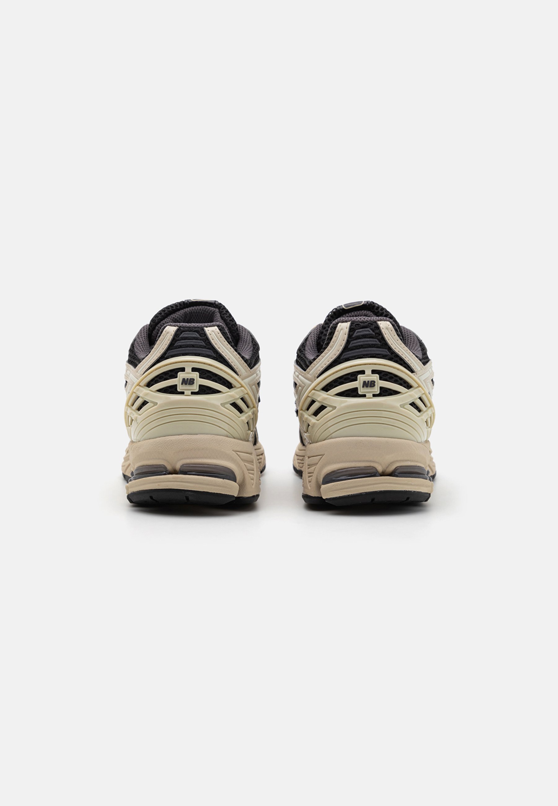 Par de zapatillas New Balance beige y negras vistas desde atrás sobre un fondo blanco liso.