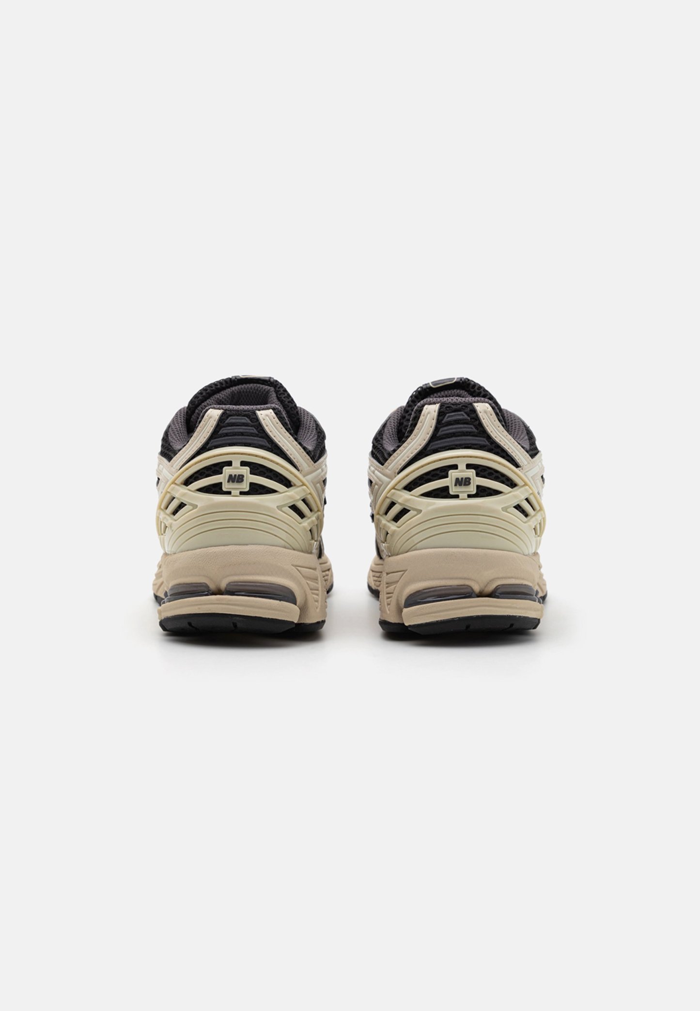 Par de zapatillas New Balance beige y negras vistas desde atrás sobre un fondo blanco liso.