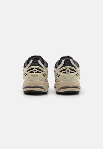 Par de zapatillas New Balance beige y negras vistas desde atrás sobre un fondo blanco liso.