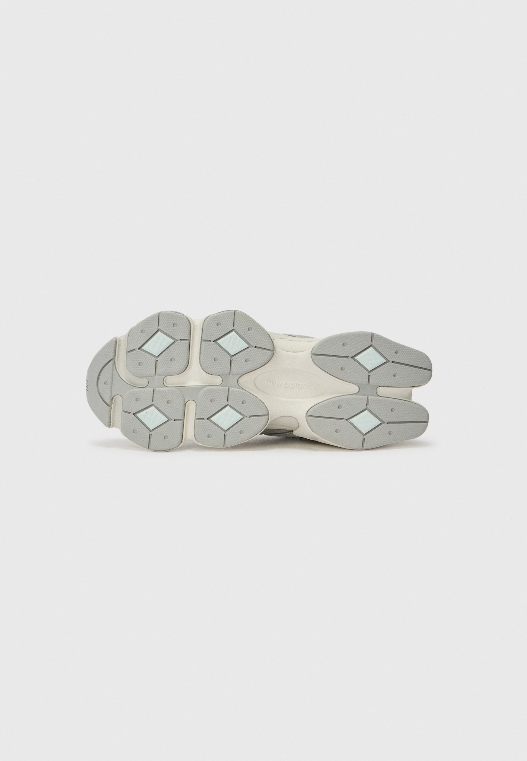 Suela de un zapato New Balance blanco y gris que muestra patrones de tracción en forma de diamante y áreas de agarre texturizado.