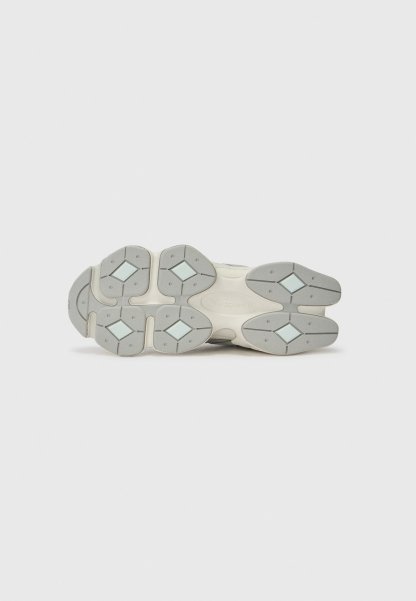 Suela de un zapato New Balance blanco y gris que muestra patrones de tracción en forma de diamante y áreas de agarre texturizado.