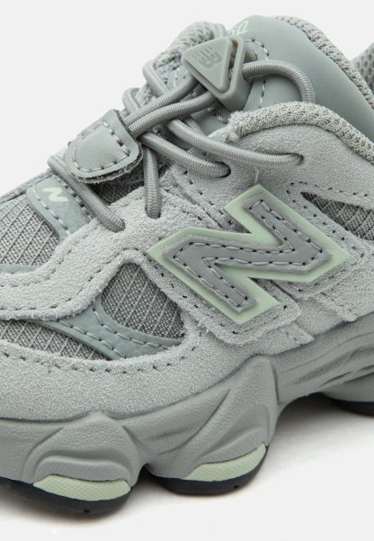 Zapatilla New Balance de color gris claro con paneles de ante y malla, costuras detalladas, cierre con cordones y suela gruesa y texturizada.