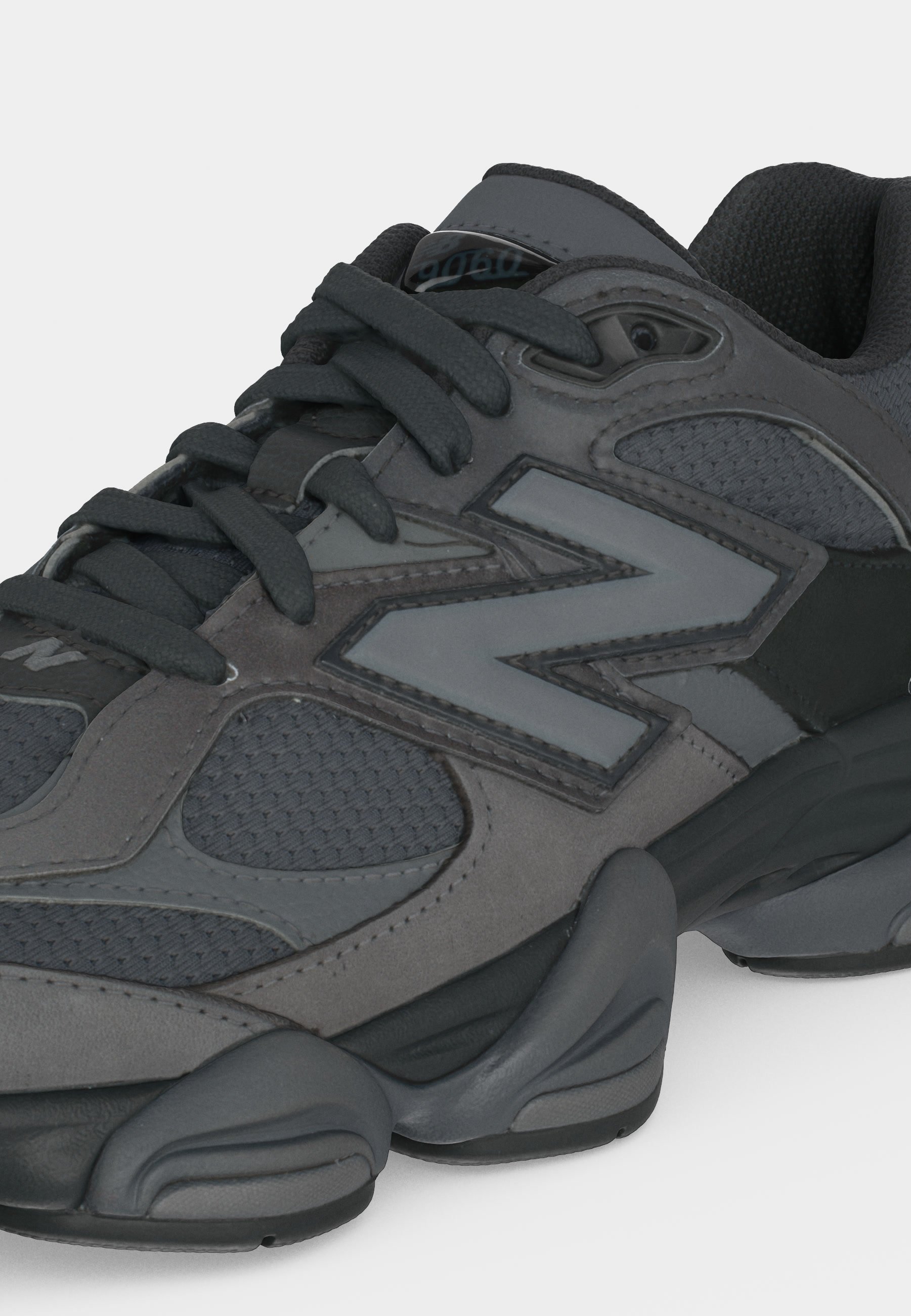 Zapatilla deportiva gris oscuro y negra con paneles de malla, suela gruesa y gran logo "N" en el lateral, vista desde el frente lateral.
