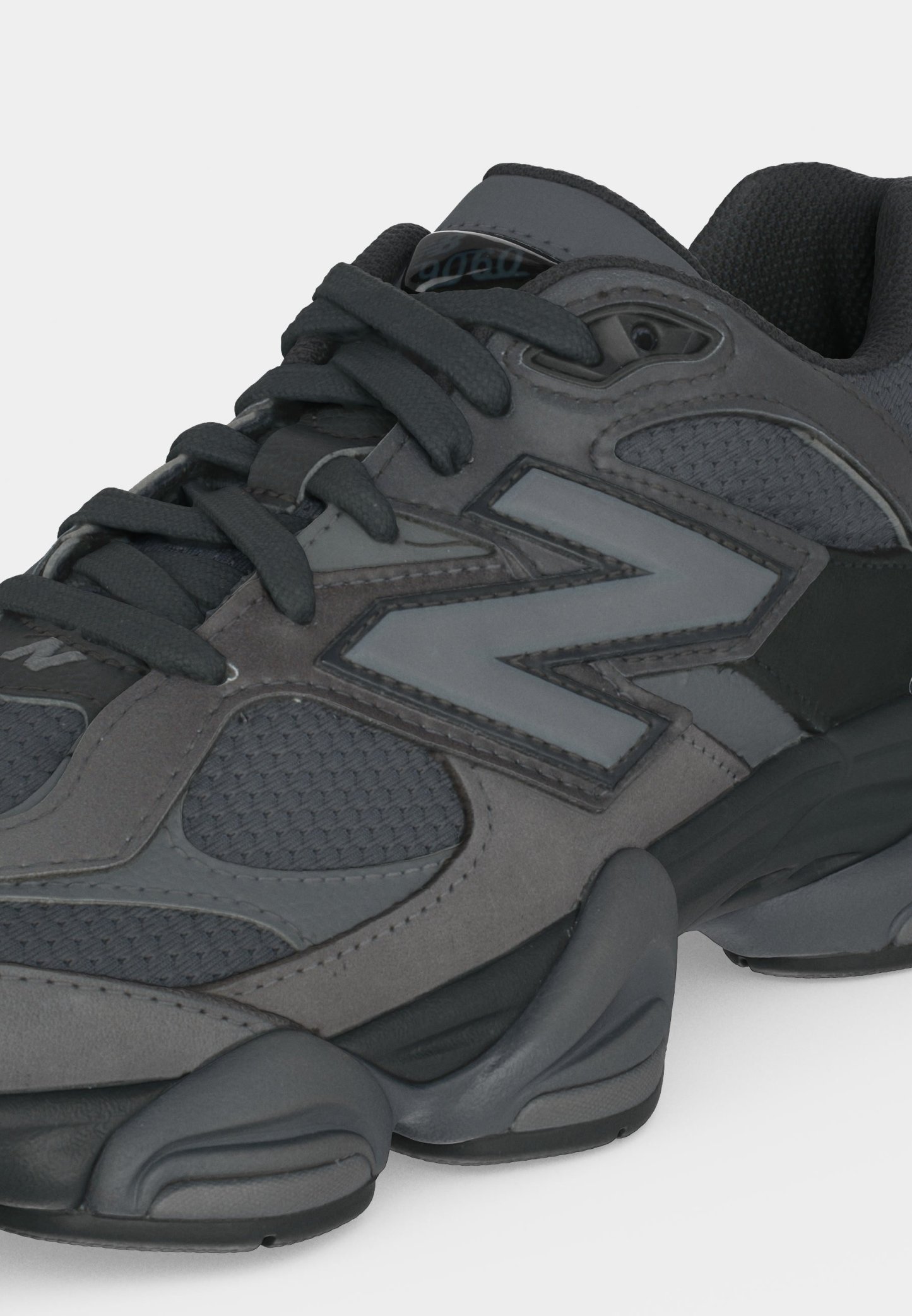 Zapatilla deportiva gris oscuro y negra con paneles de malla, suela gruesa y gran logo "N" en el lateral, vista desde el frente lateral.