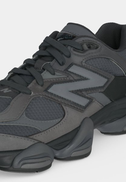 Zapatilla deportiva gris oscuro y negra con paneles de malla, suela gruesa y gran logo "N" en el lateral, vista desde el frente lateral.