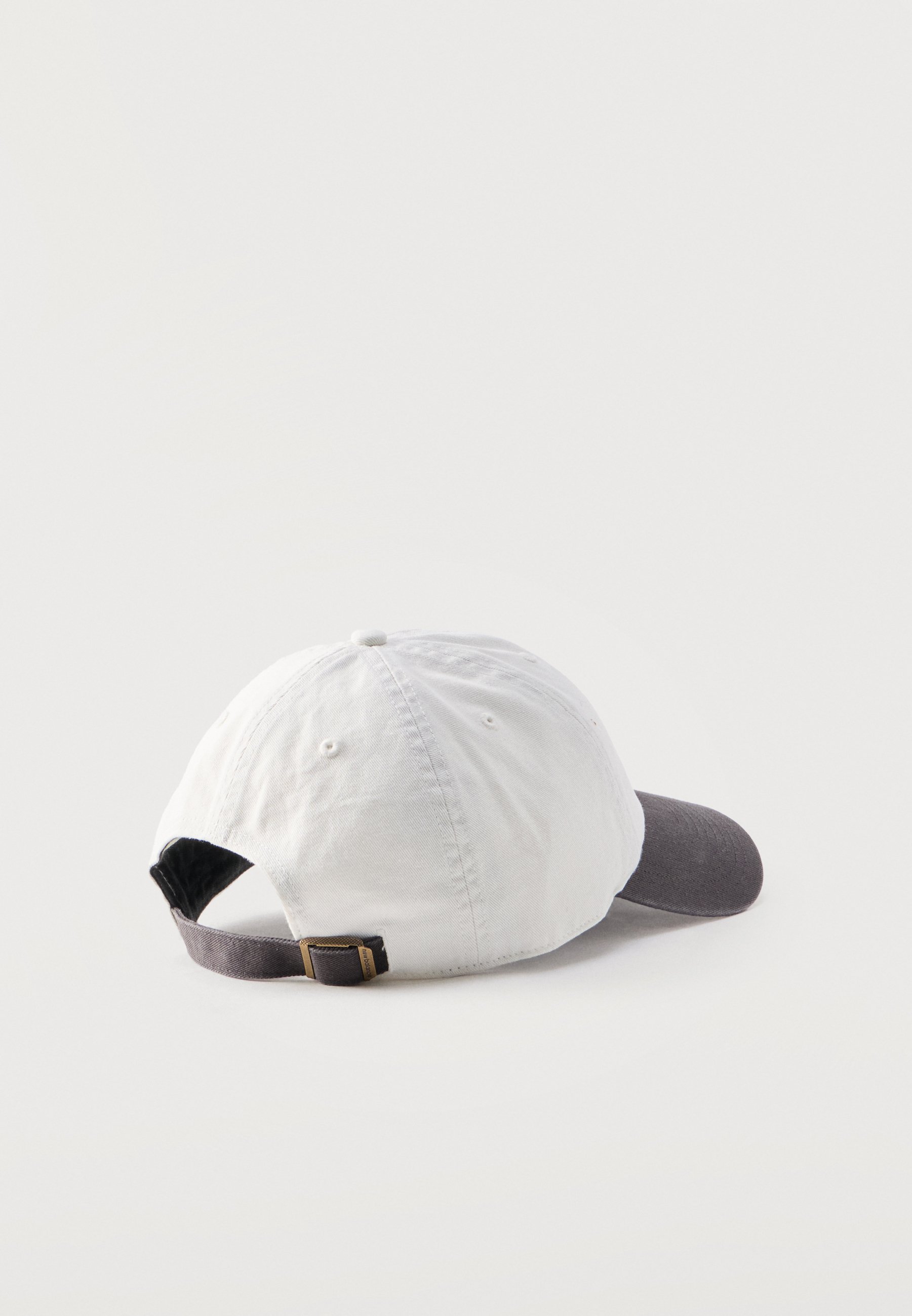 Gorra de béisbol blanca con visera curva gris oscuro y correa ajustable con hebilla metálica, mostrada desde atrás sobre un fondo claro.
