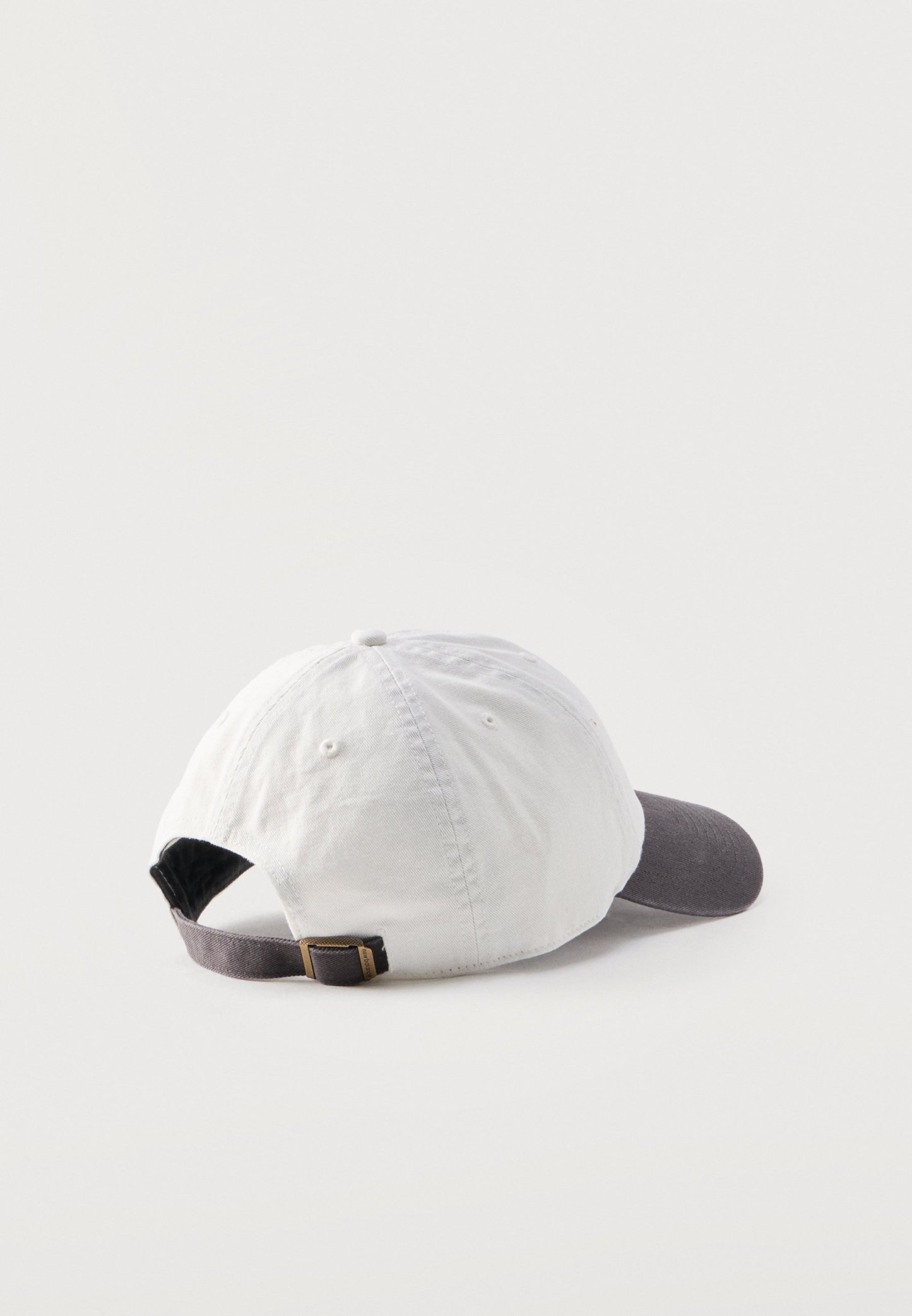 Gorra de béisbol blanca con visera curva gris oscuro y correa ajustable con hebilla metálica, mostrada desde atrás sobre un fondo claro.