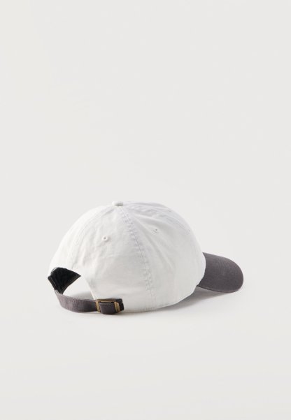 Gorra de béisbol blanca con visera curva gris oscuro y correa ajustable con hebilla metálica, mostrada desde atrás sobre un fondo claro.