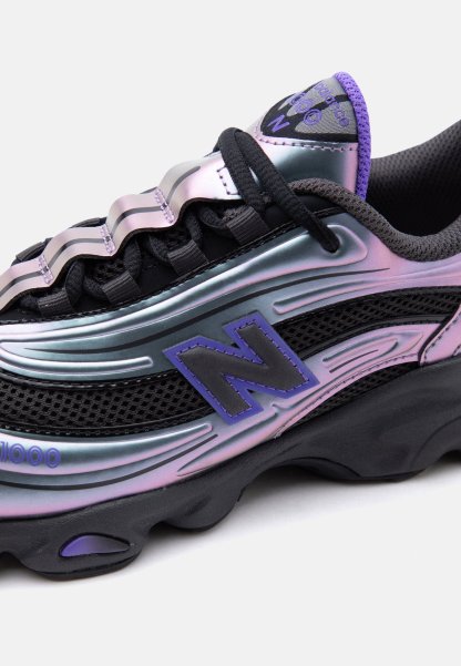Zapatilla New Balance negra e iridiscente en púrpura con suela gruesa, paneles de malla, superposiciones con forma de onda y cordones negros.