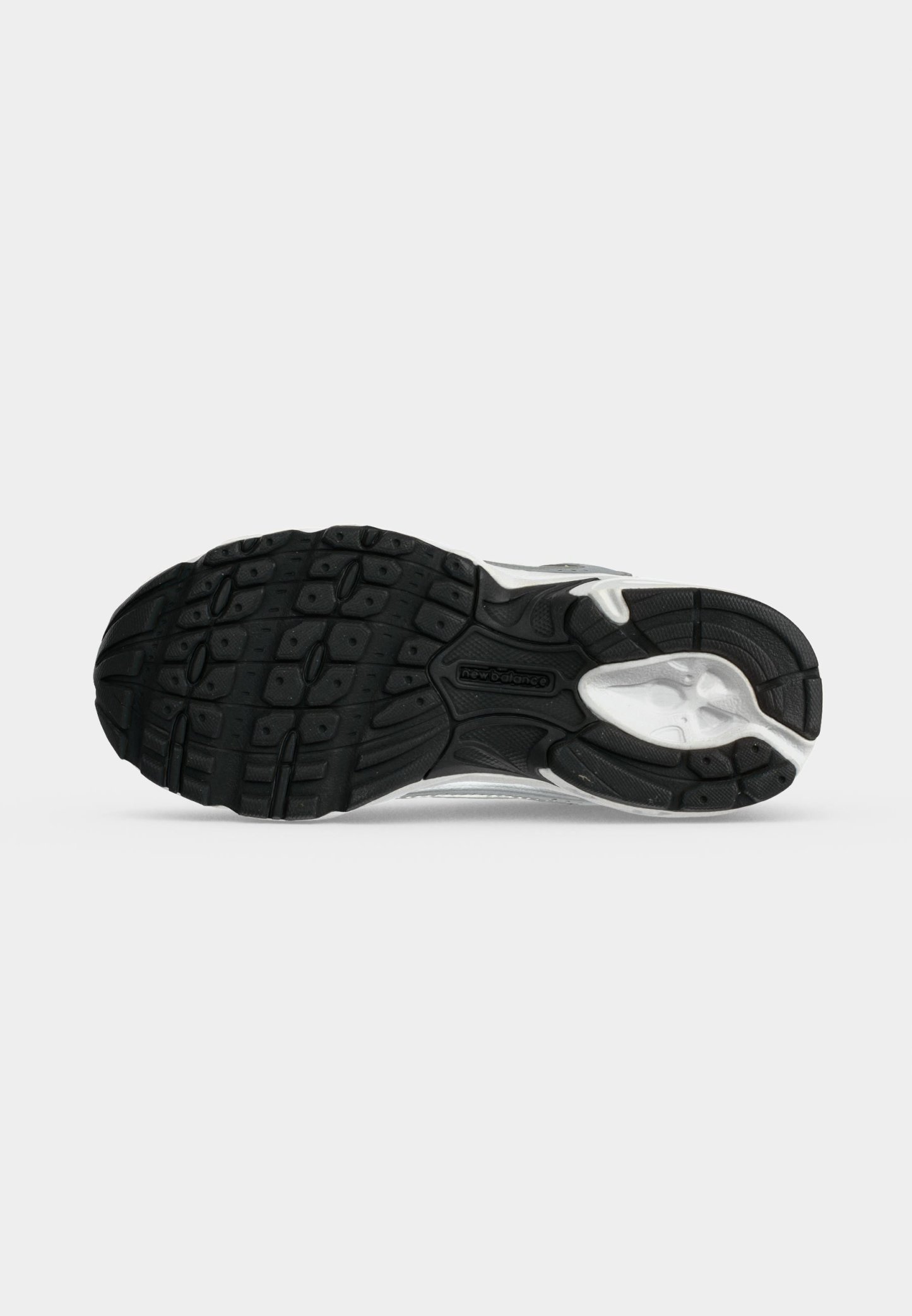 Suela de zapato deportivo en blanco y negro con tacos texturizados y logo de New Balance en el centro, vista desde abajo sobre fondo blanco.