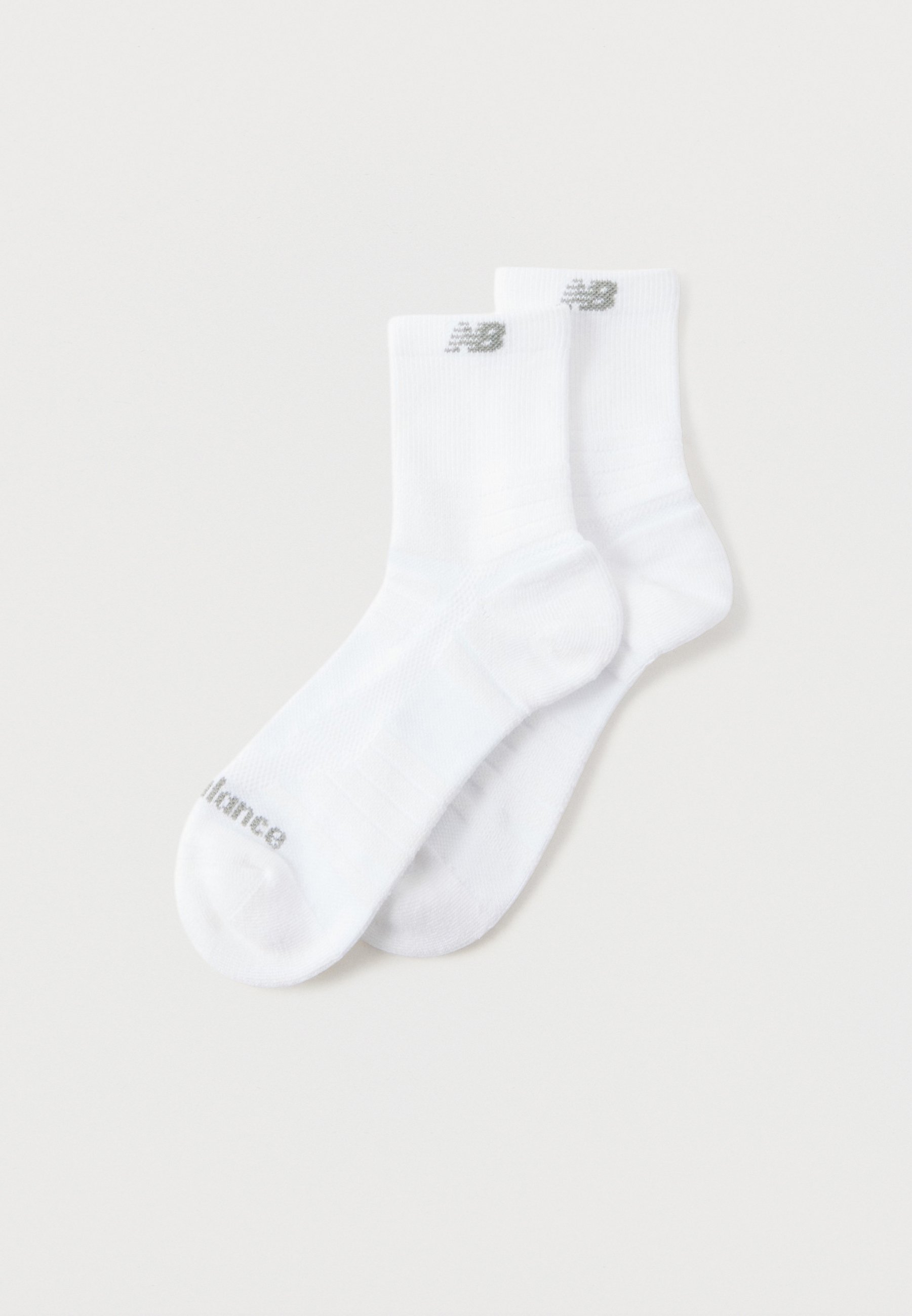 Par de calcetines blancos hasta el tobillo con el logo gris de New Balance en los puños y texto en las puntas, colocados extendidos sobre un fondo claro.