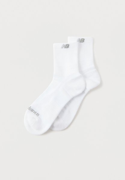 Par de calcetines blancos hasta el tobillo con el logo gris de New Balance en los puños y texto en las puntas, colocados extendidos sobre un fondo claro.