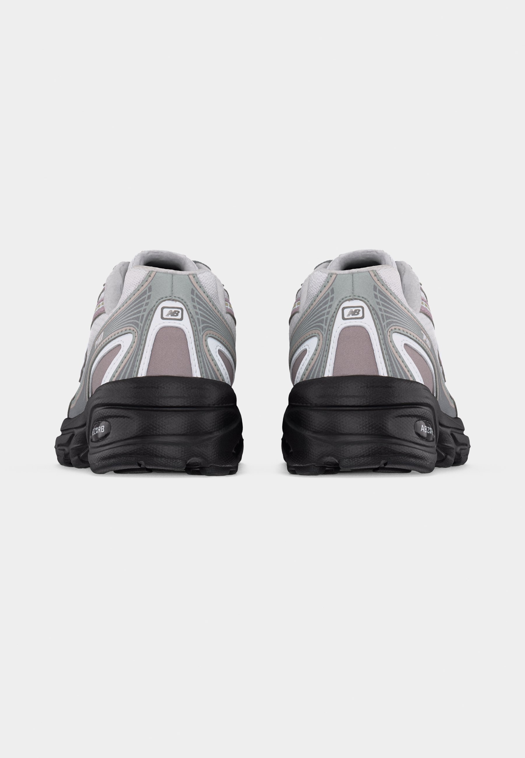 Par de zapatillas deportivas gris y blancas con suelas negras, vistas desde atrás sobre un fondo liso de color gris claro.