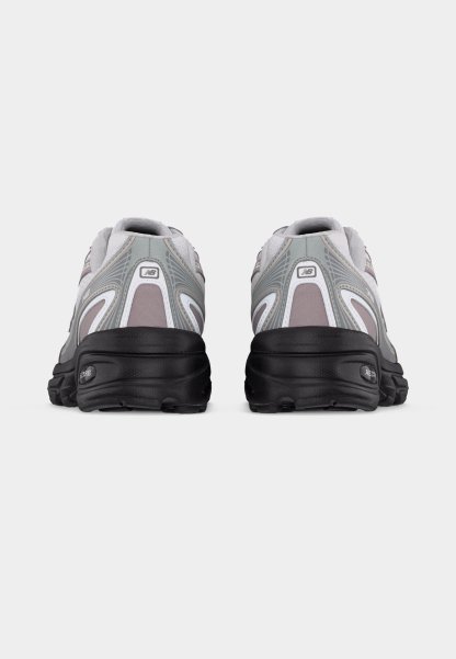 Par de zapatillas deportivas gris y blancas con suelas negras, vistas desde atrás sobre un fondo liso de color gris claro.