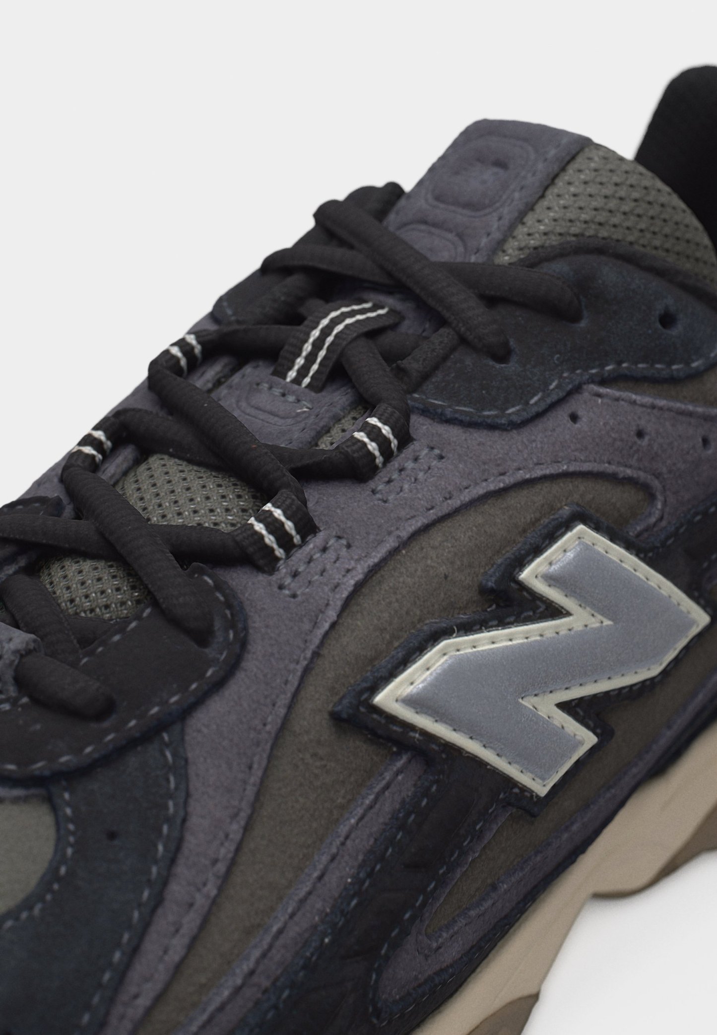 Zapatilla negra y gris con paneles de malla y ante, cordones negros con rayas blancas y un logotipo "N" reflectante en gris en el costado.
