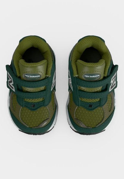 Par de zapatillas para niños pequeños New Balance verdes y verde oscuro con tiras de velcro y tejido de malla, mostradas desde arriba sobre un fondo blanco.