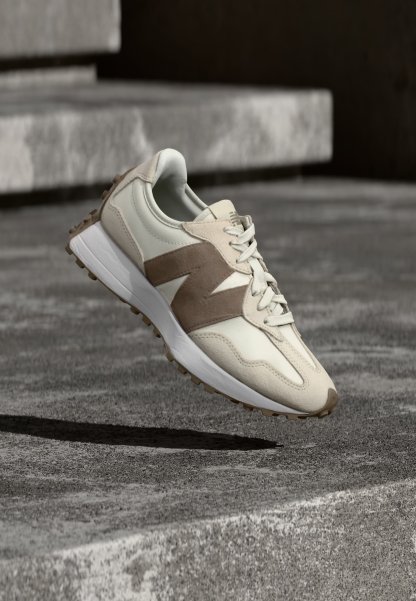 Zapatilla deportiva de color beige claro y marrón con una suela blanca gruesa, flotando sobre una superficie de hormigón texturizada y escalones con iluminación suave.