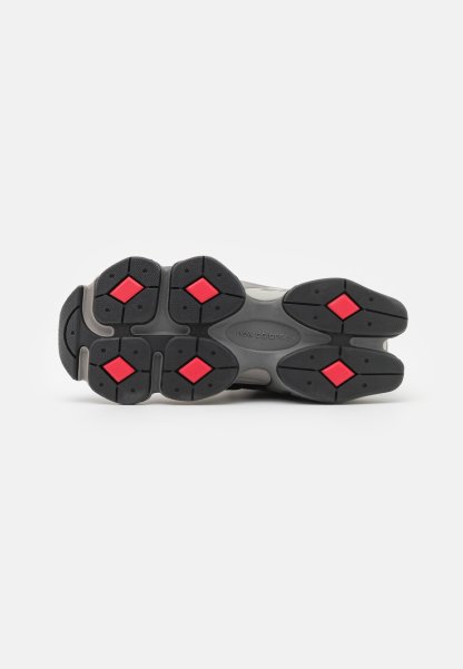 Suela de zapato de goma negra con acentos rojos en forma de diamante, que presenta patrones de agarre texturizados y un diseño elegante y redondeado con marca visible.