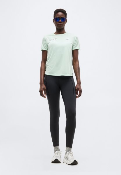 Mujer con camiseta de manga corta verde claro, leggings negros, calcetines grises, zapatillas deportivas blancas y gafas de sol deportivas azules de pie frente a un fondo liso.