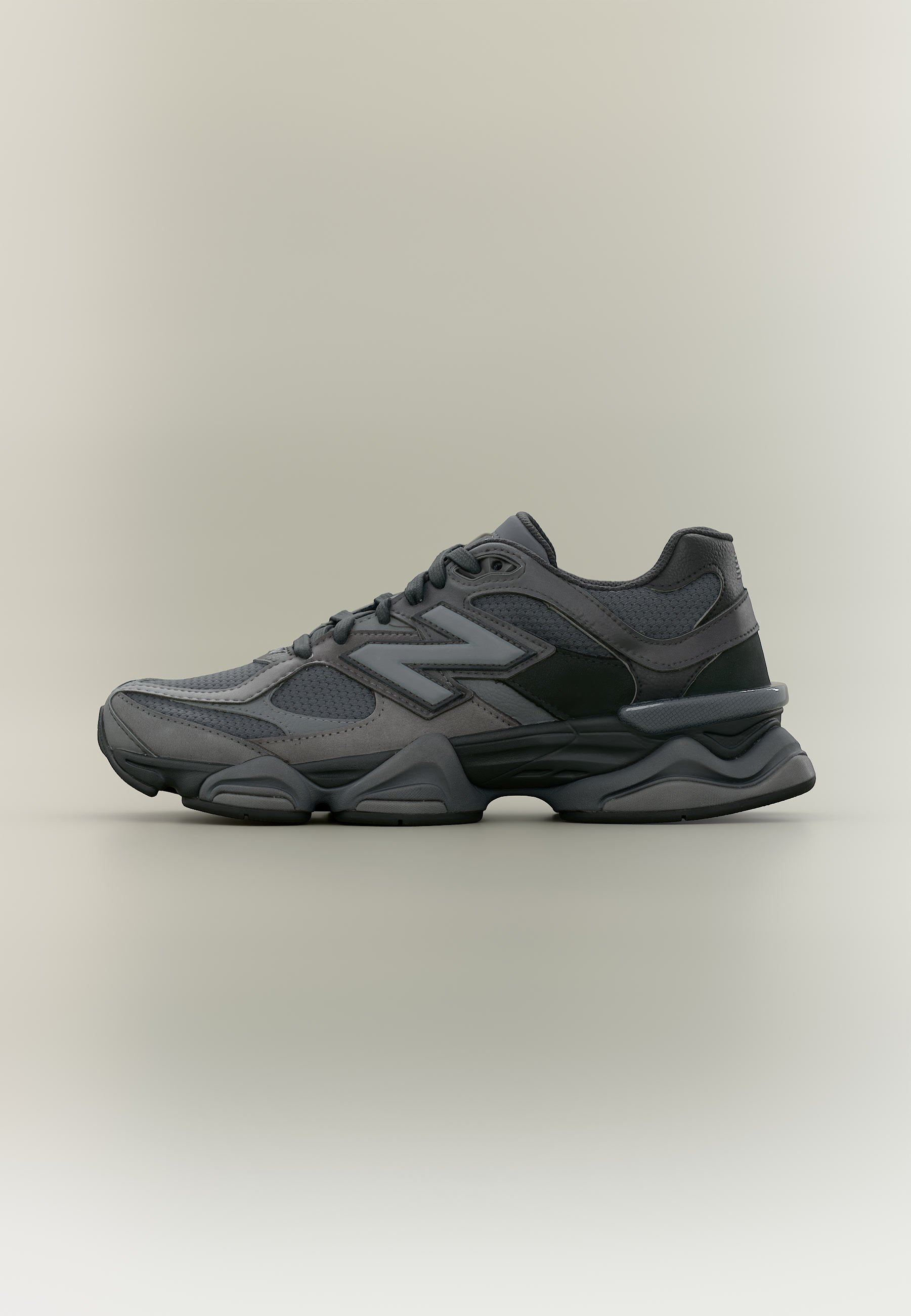 Zapatilla deportiva gris oscuro con paneles de malla y cuero, cordones en la parte delantera y suela gruesa esculpida, mostrada de perfil.