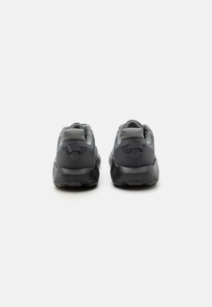 Par de zapatillas deportivas negras y grises vistas desde atrás con cuellos acolchados y detalles de tela texturizada sobre un fondo blanco.